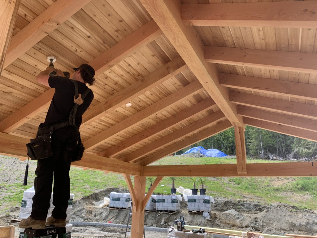 Carpenter fitting a light into the fir ceiling of a custom timber pavilion