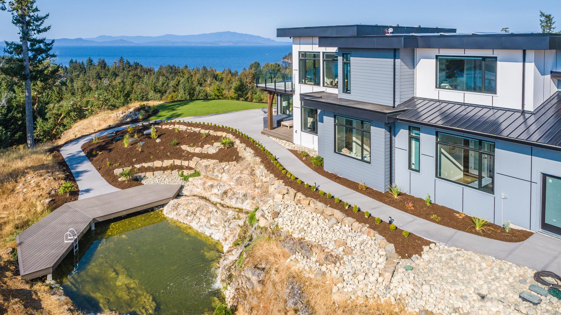 Aerial view of the home, natural pond and landscaped grounds from above the treeline