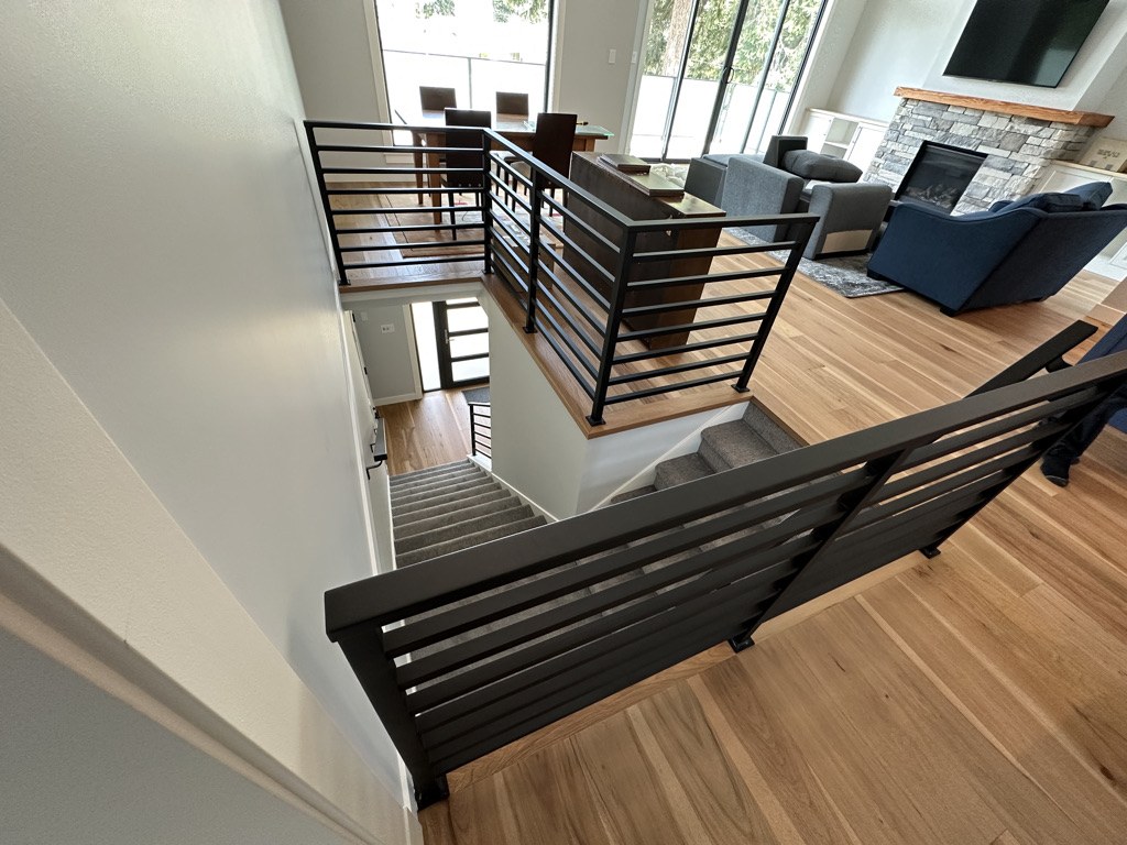 Open stairwell with a black steel railing looking down into the great room