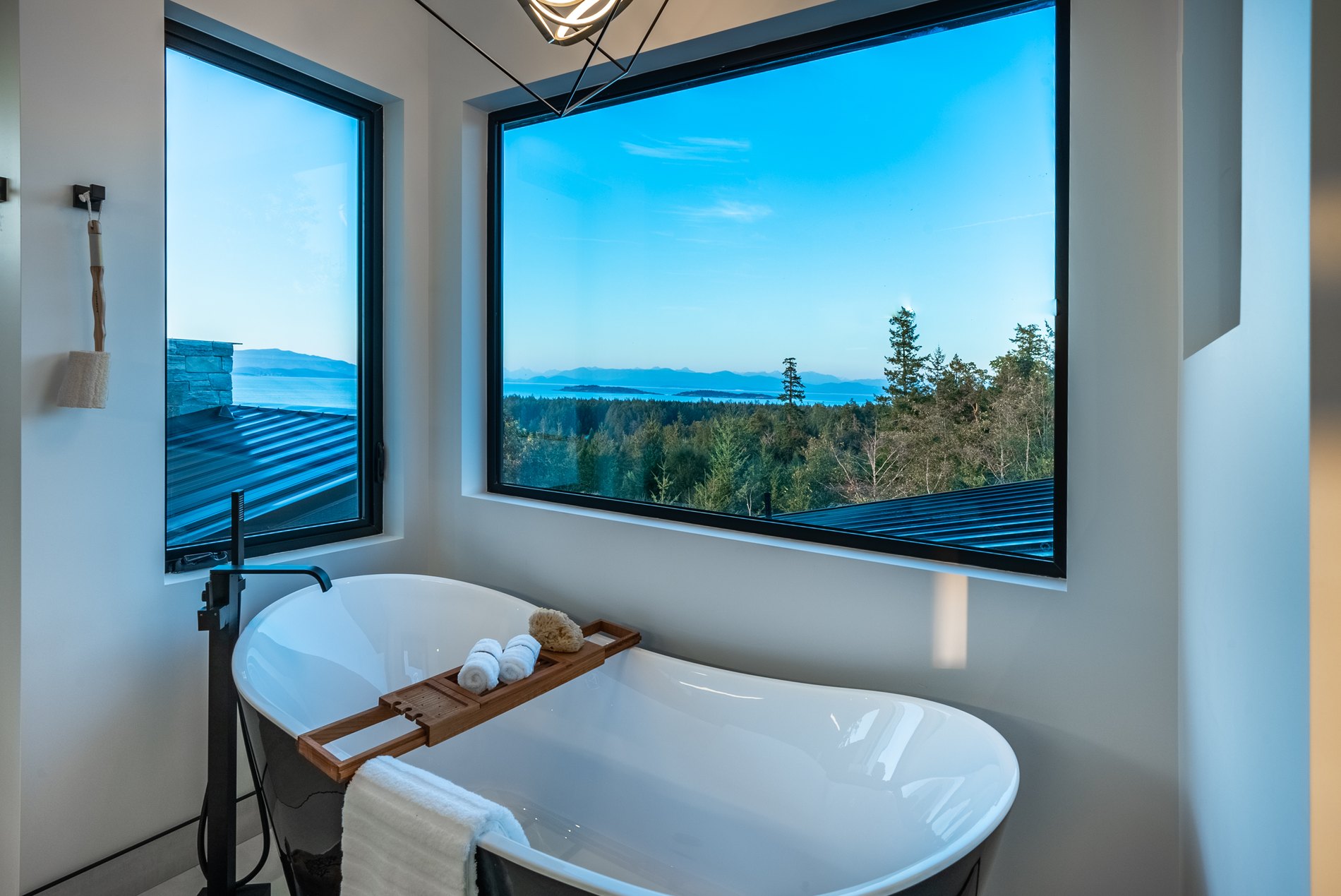 Freestanding soaker tub set beneath a large picture window with a treed view