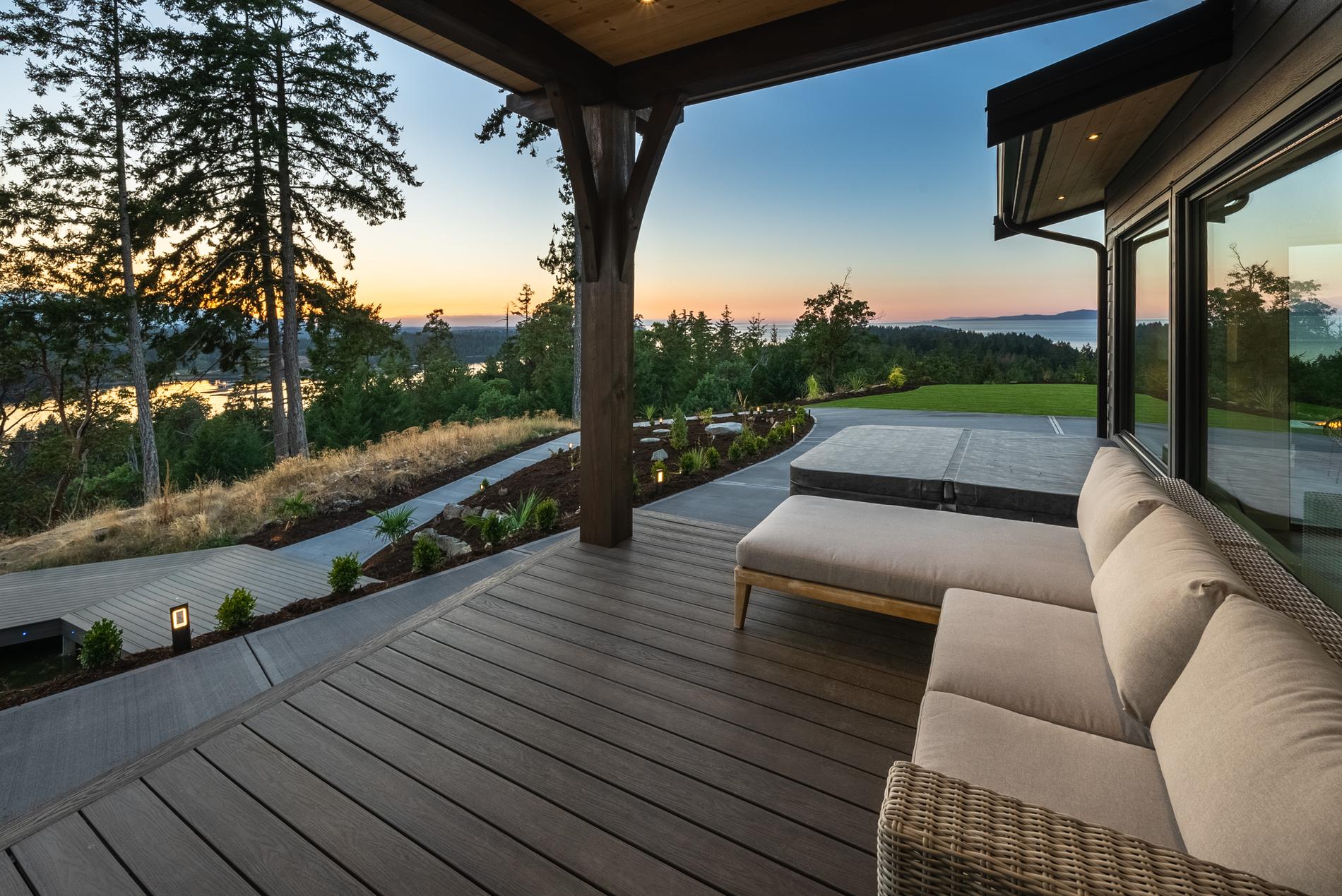 Covered deck with timber posts, outdoor sofas and an ocean view at sunset