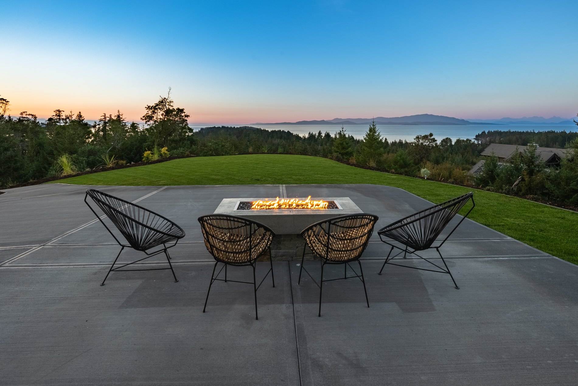 Outdoor firepit table and lounge chairs on a concrete patio at dusk